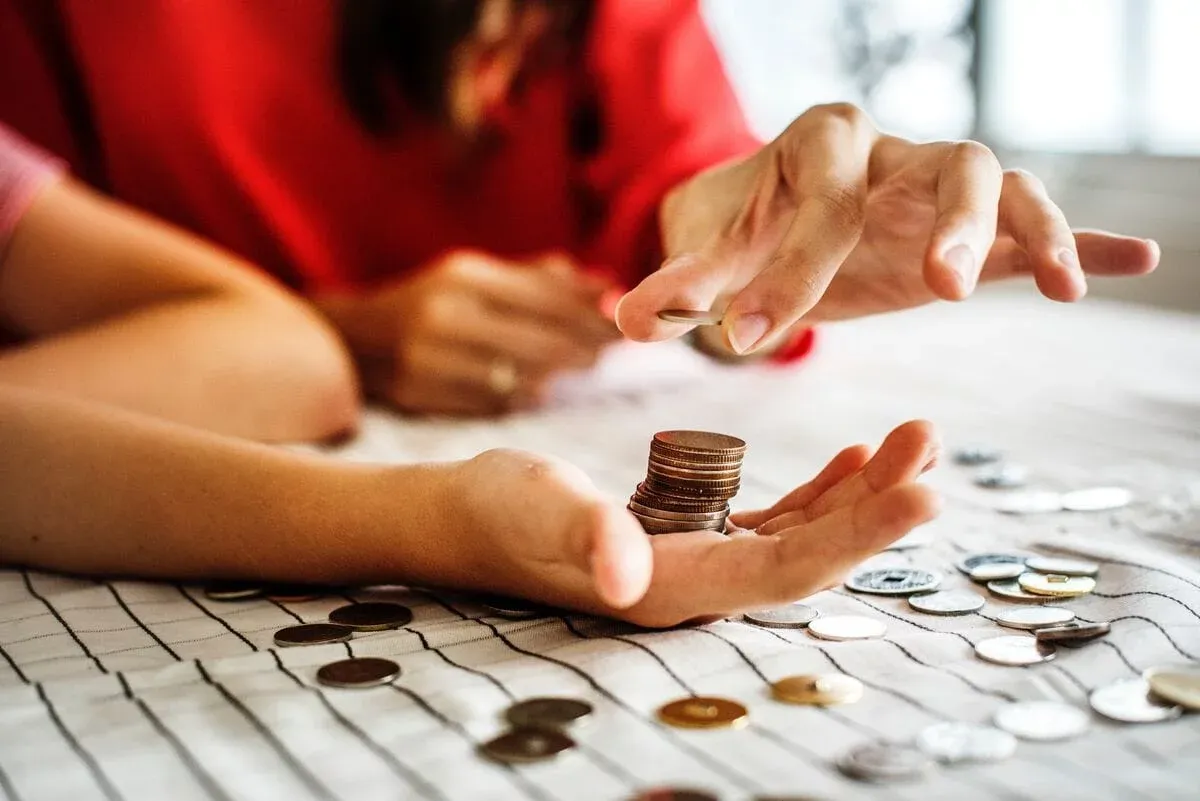 Hands counting coins on a striped tablecloth, one palm holding a small stack