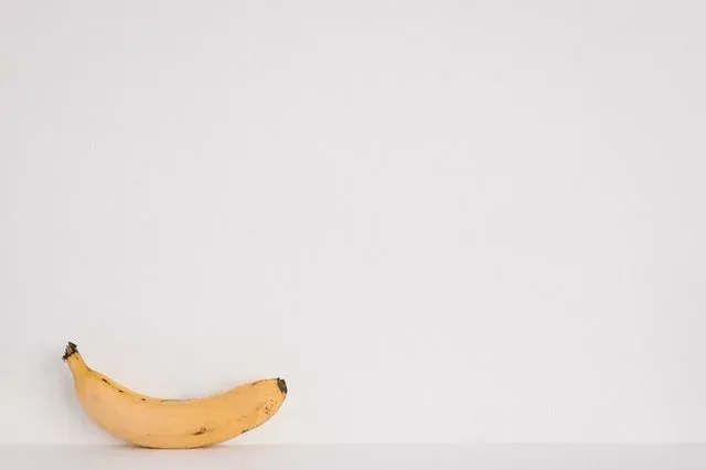 Single ripe banana with brown spots against a plain white wall