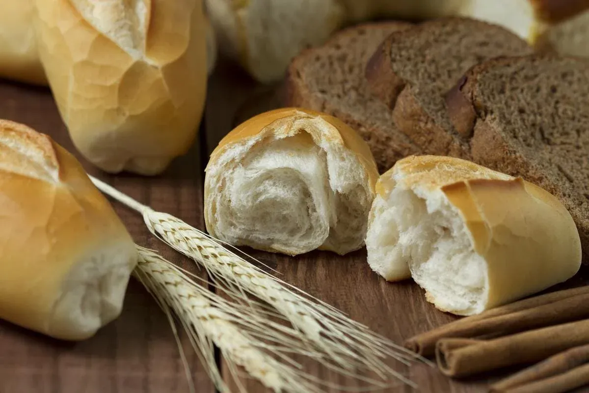 White rolls, sliced dark bread, wheat ears and cinnamon sticks on wood