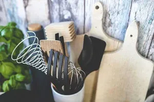 Spatules et fouets dans un pot, à côté de planches à découper en bois