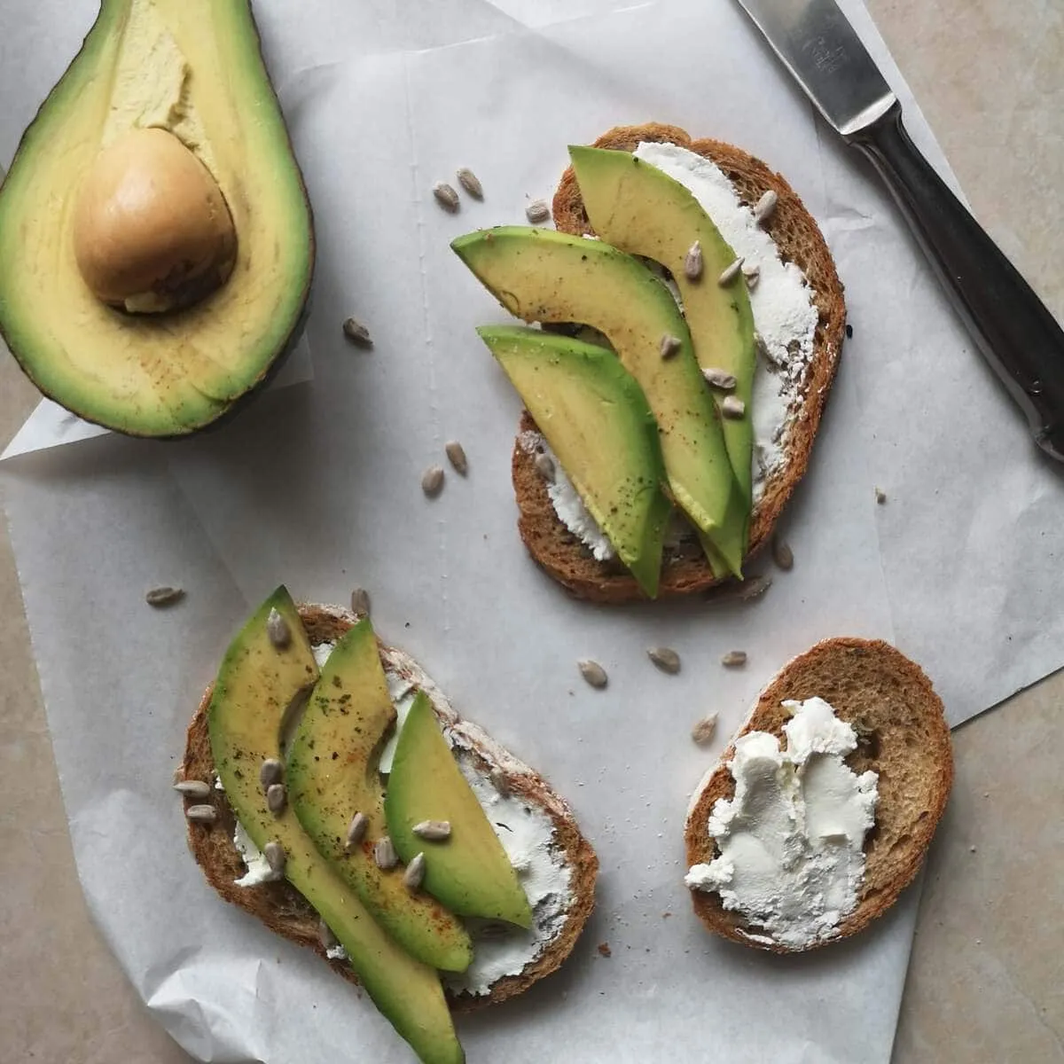 Tartines au fromage frais et tranches d’avocat, avec un demi-avocat