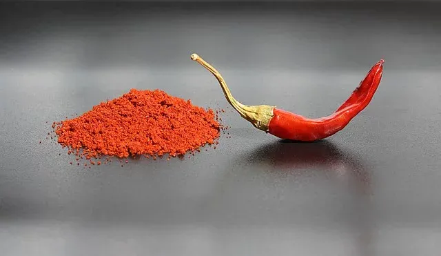 Papryczka chili i stosik czerwonej przyprawy w proszku na ciemnym blacie