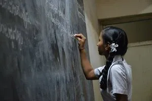 Écolière aux cheveux noués écrivant à la craie sur un tableau noir