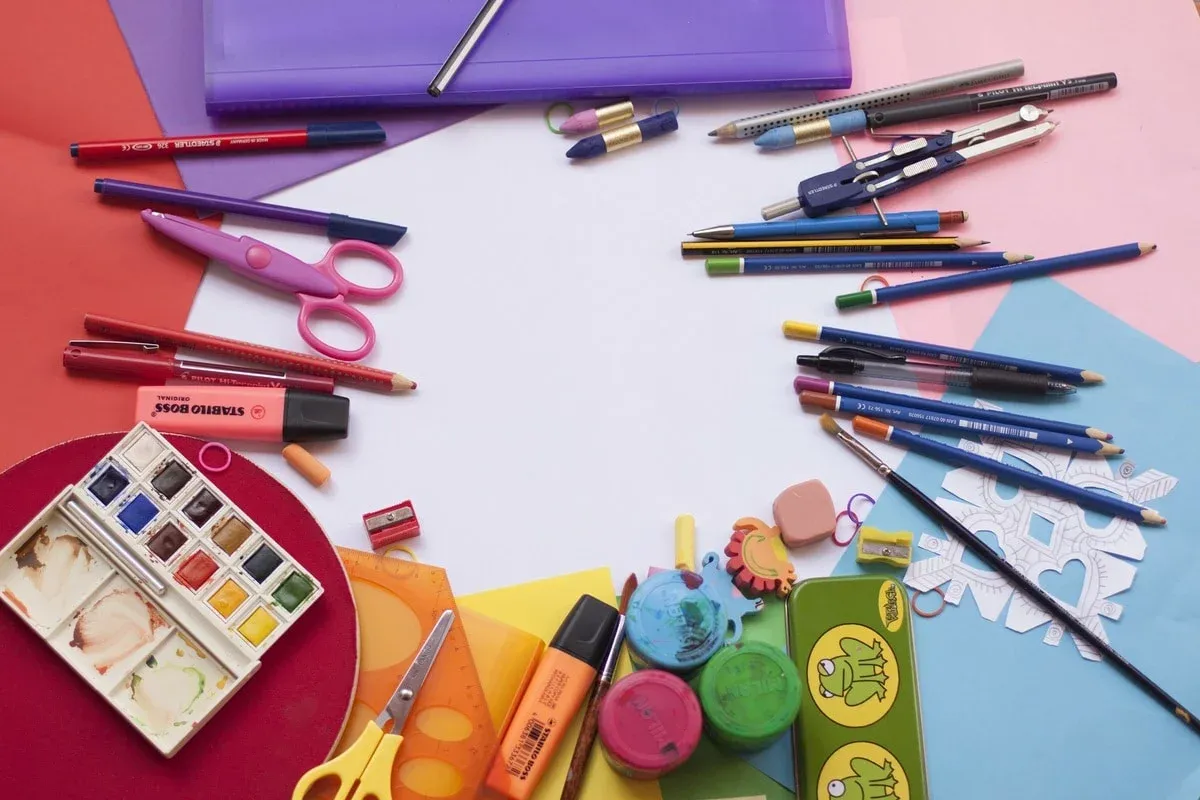 Crayons, ciseaux, surligneurs, peinture et règle autour d’une feuille blanche