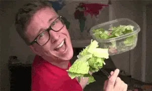 Homme à lunettes brandissant une feuille de laitue et une boîte de salade