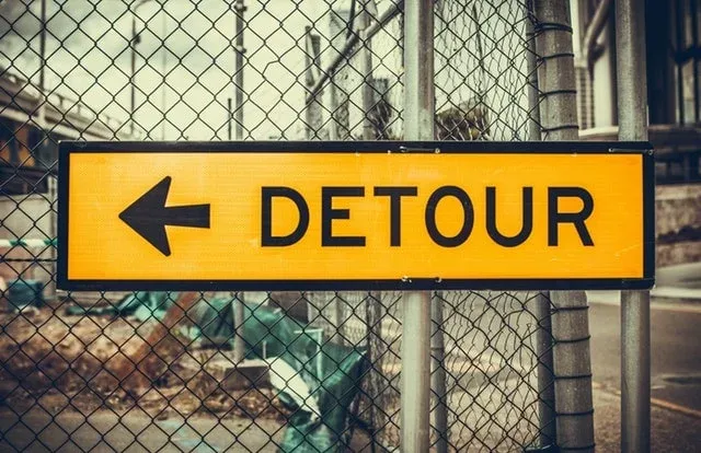 Panneau jaune Detour avec une flèche vers la gauche devant un grillage