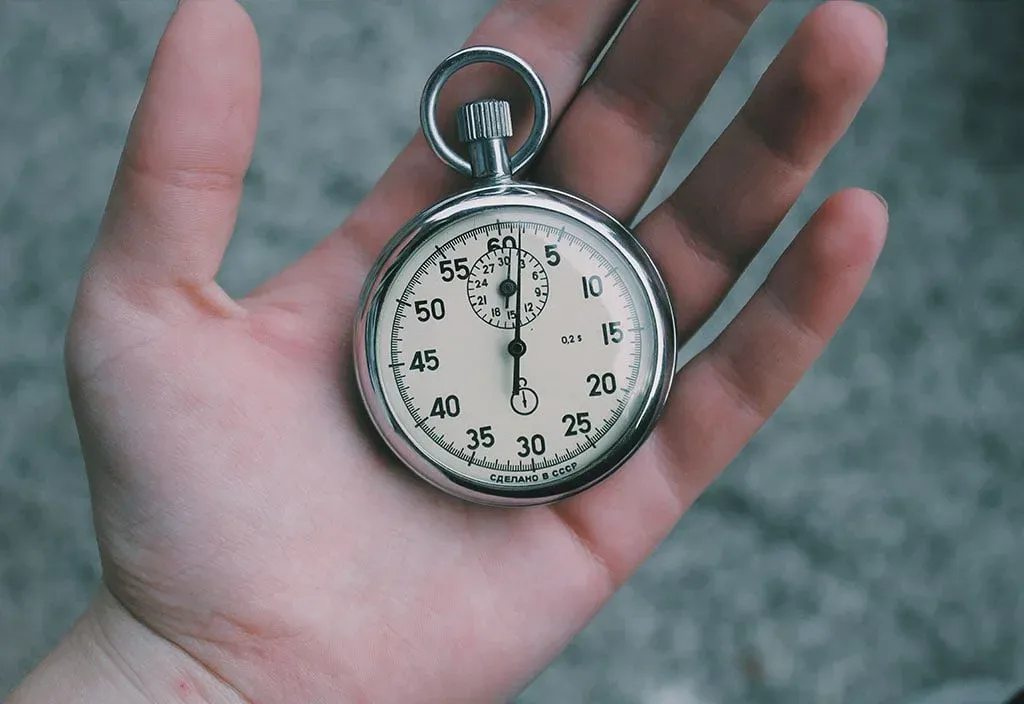 An open palm holding a silver stopwatch with a cream dial