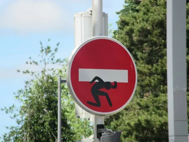 Panneau de sens interdit rouge détourné avec un personnage portant la barre