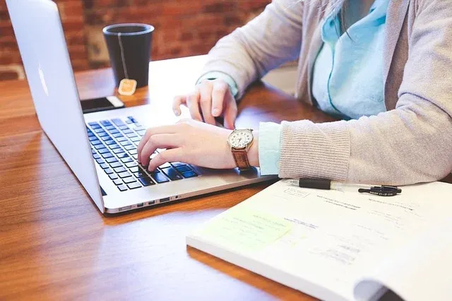 Mains sur le clavier d'un ordinateur portable, avec un cahier et une tasse