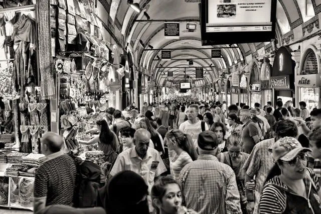A crowded covered market hall packed with shoppers, in black and white