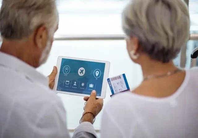 An older couple looking at a travel booking on a tablet, boarding passes in hand